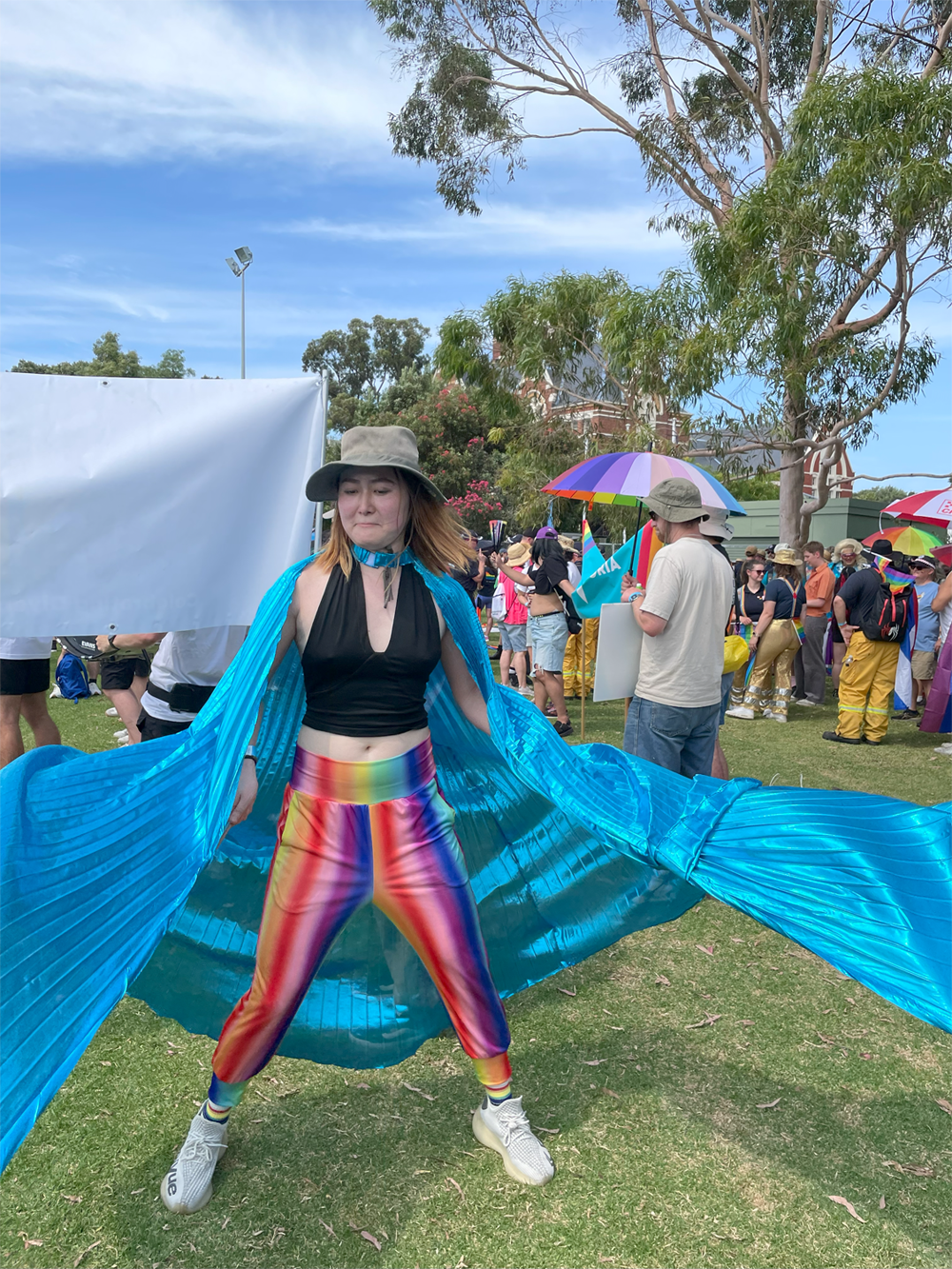Marcher in rainbow pants actively soaring giant blue winged cape