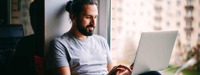 A person sitting on a window sill using a laptop