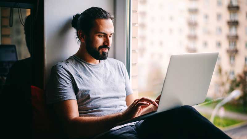 A person sitting on a window sill using a laptop