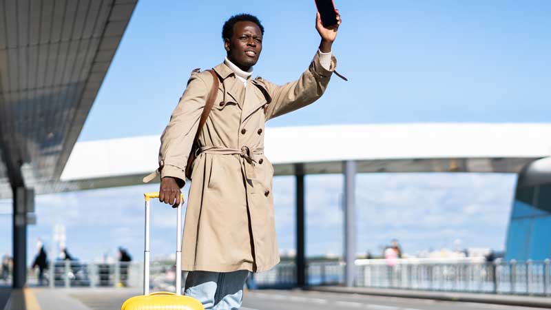A person with a suitcase raising an arm to hail a taxi at an airport