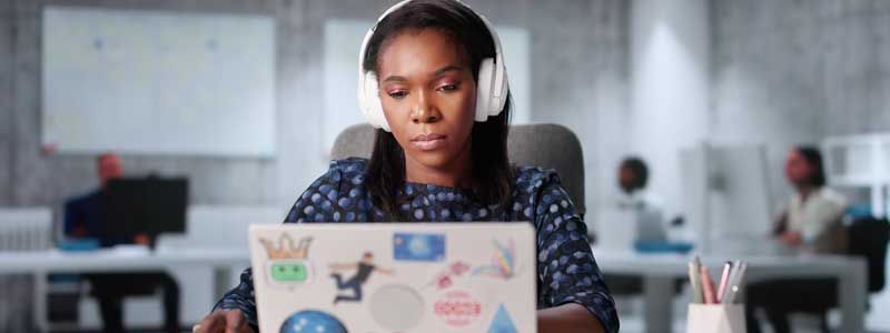 A person wearing headphones concentrating on looking at a laptop