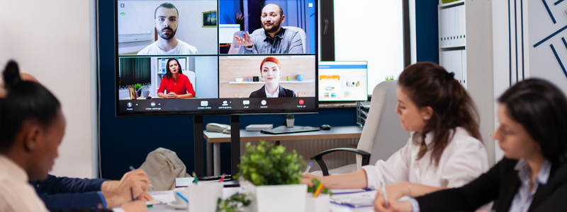 A group of people in a meeting room, with people on a screen